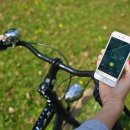 Fahrradfahrer mit Handy in der Hand, auf dem eine App gezeigt wird.