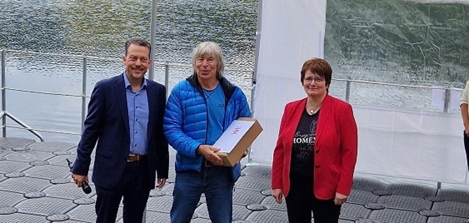 Bürgermeister Tore Florin überreicht die Dankesurkunde des Hessischen Ministers des Innern und für Sport im Rahmen der Sportlerehrung der Gemeinde Fuldatal am 23. August 2025 auf der Wasserbühne am Fuldaufer in Wilhelmshausen an den Sportcoach Bernd Quast im Beisein der Vorsitzenden der Gemeindevertretung Frau Stefanie Roß-Stabernack.