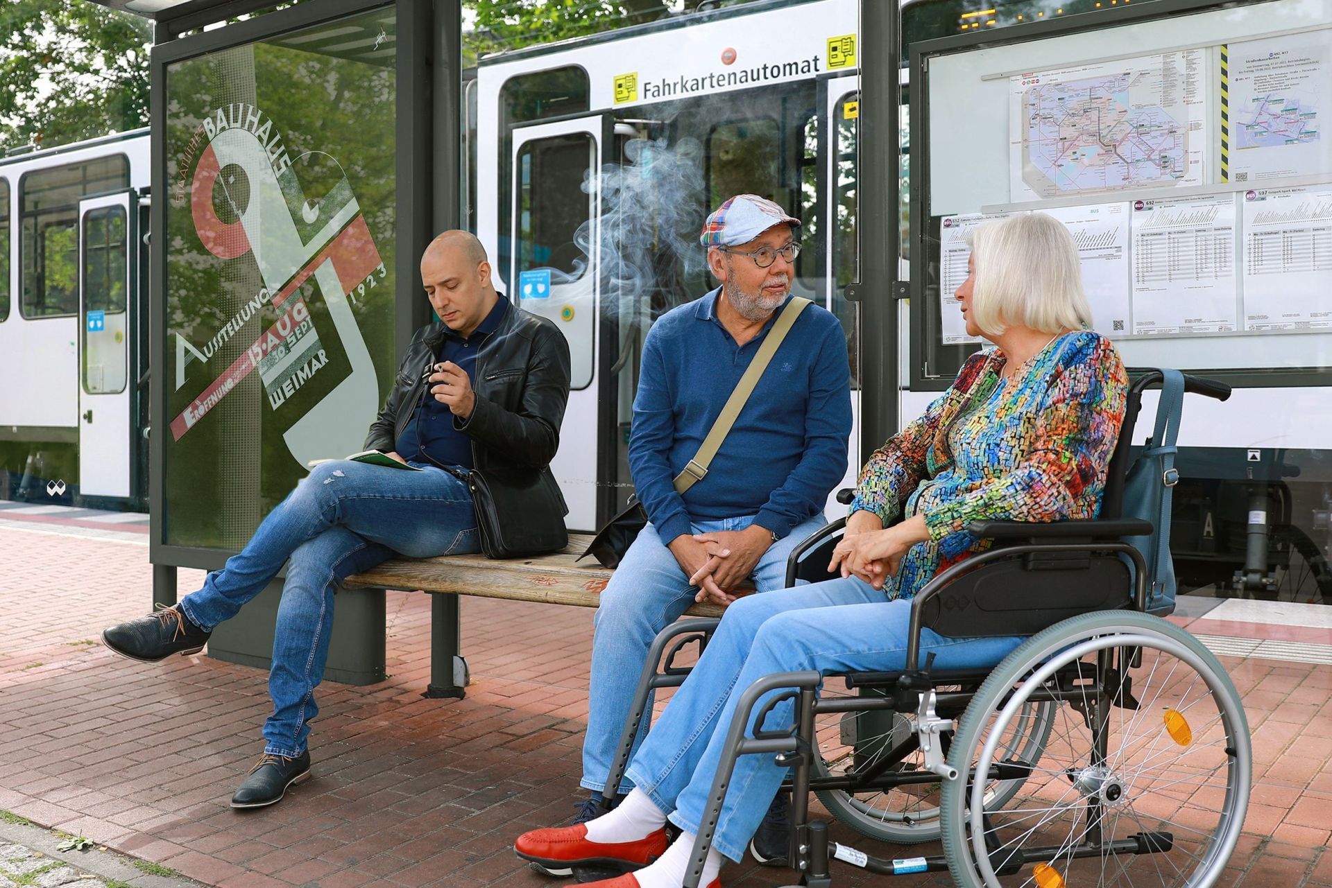 Mann unterhält sich an einer Haltestelle mit einer Frau im Rollstuhl Mann unterhält sich an einer Haltestelle mit einer Frau im Rollstuhl