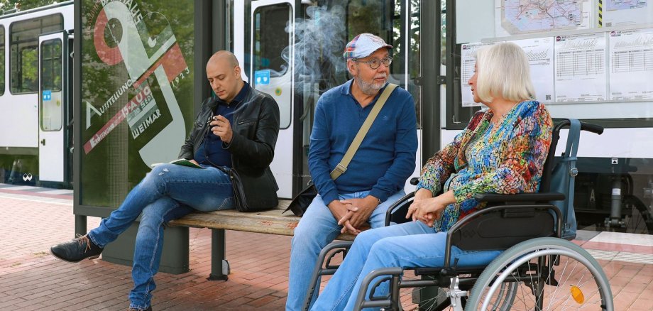 Mann unterhält sich an einer Haltestelle mit einer Frau im Rollstuhl