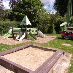 Bild vom Außengelände mit Sandkasten, Klettergerüst und Bollerwagen der Nestgruppe