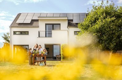 Familie vor Einfamilienhaus mit PV Anlage